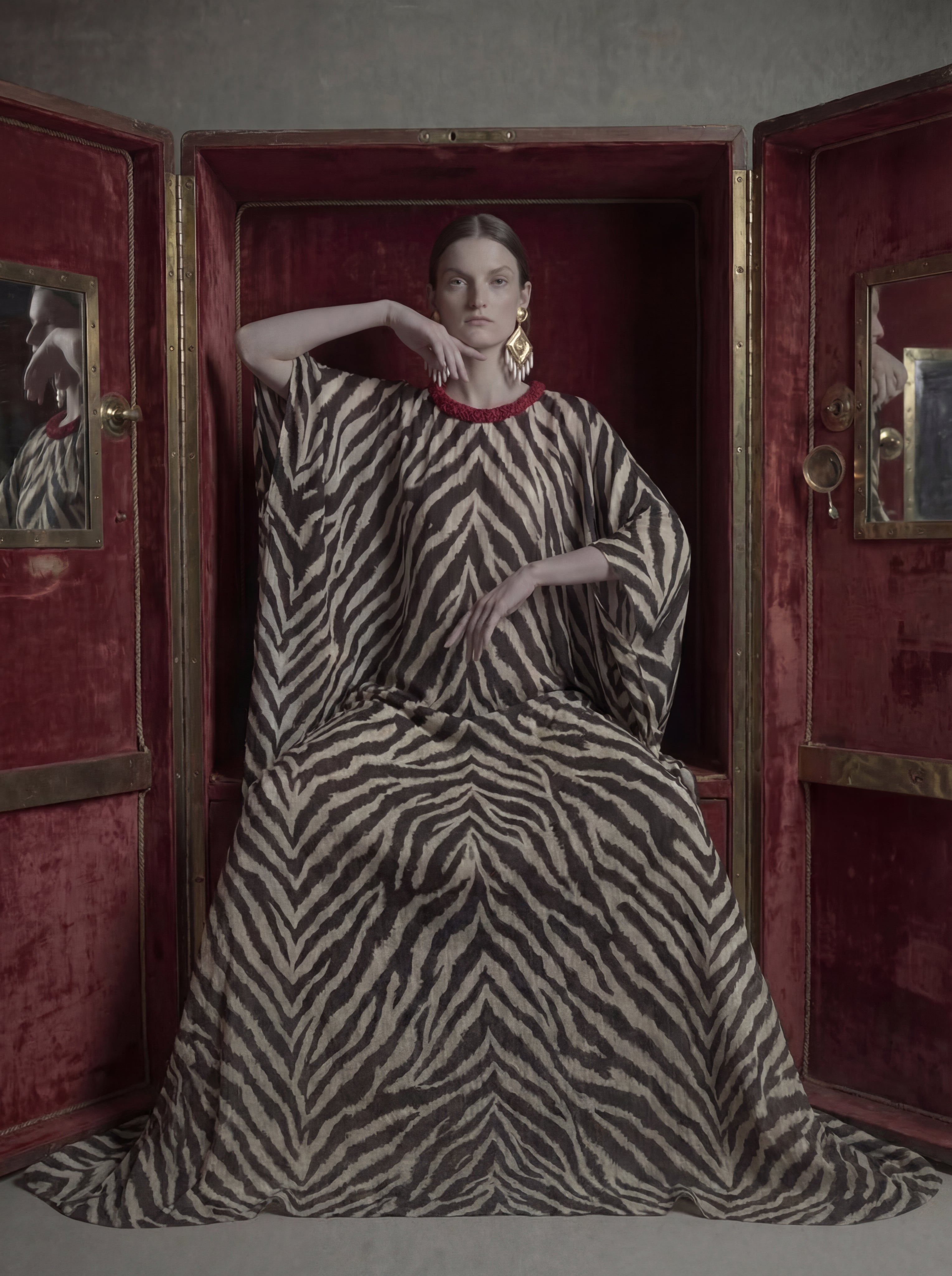 Woman in a zebra-patterned dress standing inside an ornate red cabinet.
