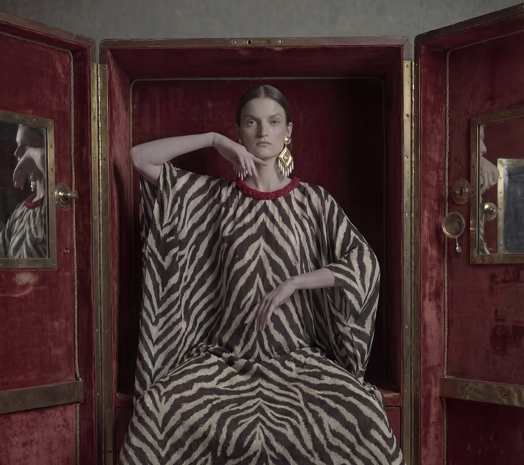 A woman wearing a striped dress sitting on a chair as a sneak peek to the collection