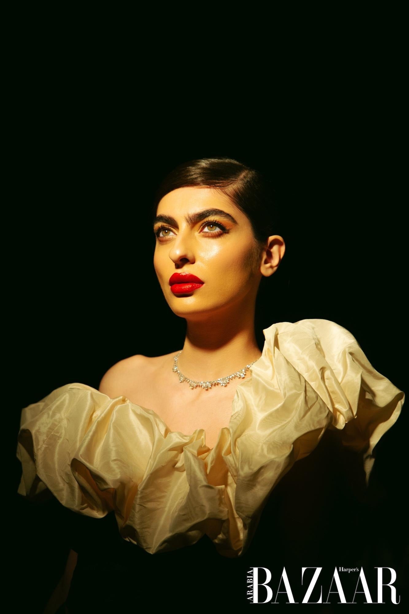 Woman wearing a white blouse with puffed sleeves against a black background, featuring the Harper's Bazaar logo.
